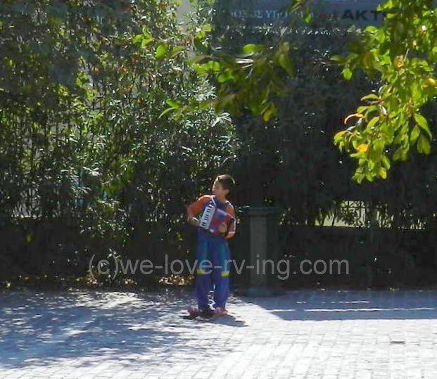 young man plays an accordian with hat on sidewalk to collect coins