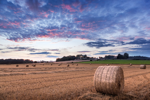 Colourful sunset colour above a Cotswold field of hay bales by Martyn Ferry Photography