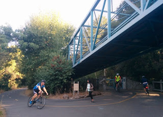 Three cyclists and a pedestrian at the south end of the bridge over Evelyn, Central, and the railroad tracks, Mountain View, California