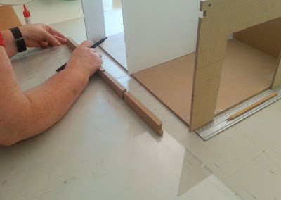 Person measuring and marking a piece of perspex against a beam.