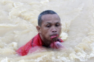 A man bites down on a plastic bag containing his belongings as he wades through a flooded street in Marikina,