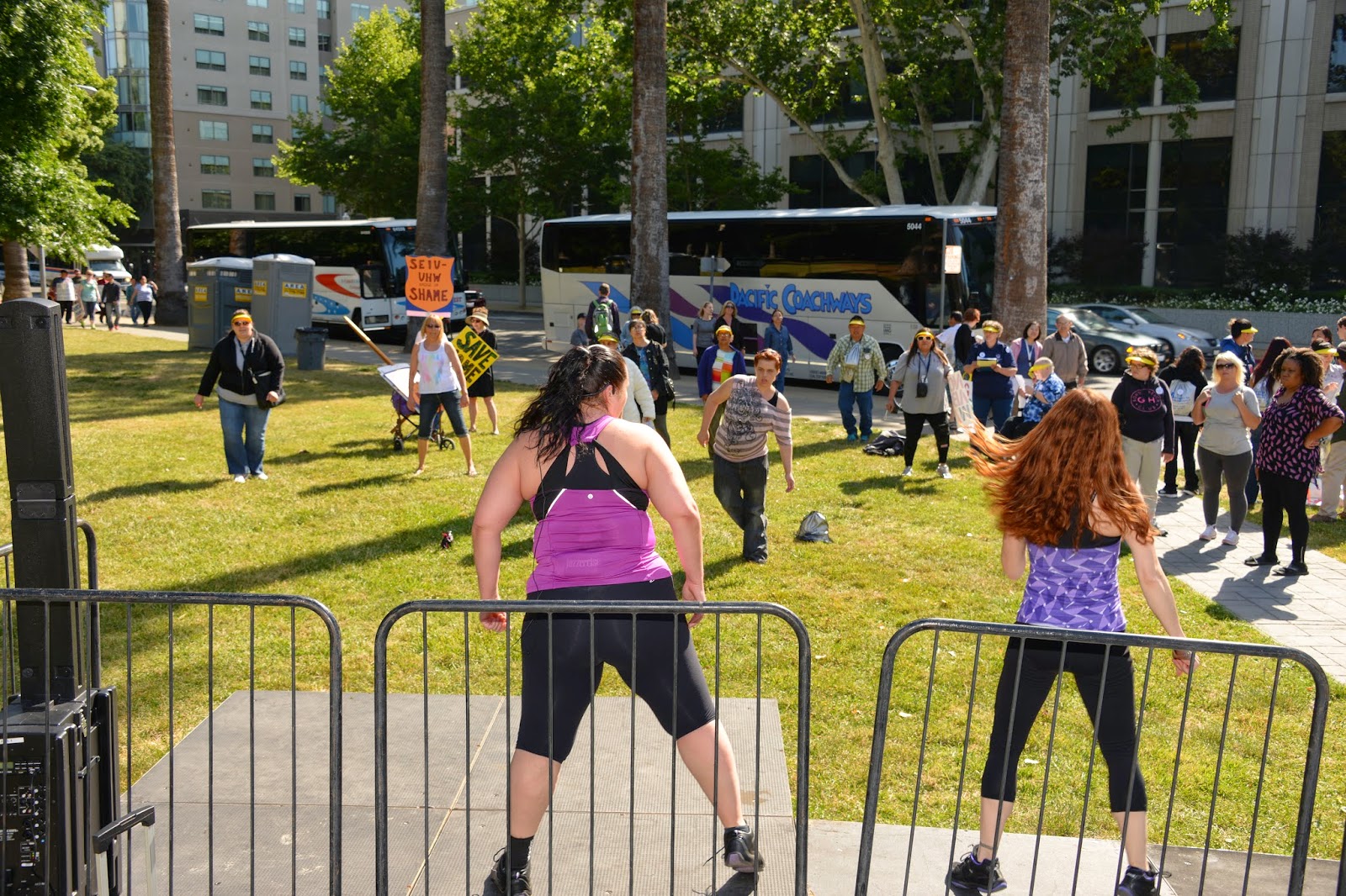 two women lead a group of people in an outdoor exercise routine.