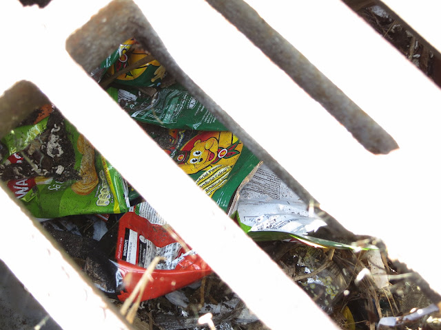 Bright wrappers and other rubbish seen through the cover of a drain in a gutter.