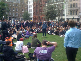 A crowd of a couple of hundred people sitting in a horseshoe shape around Josie Long who is performing. In the foreground there's the backs of me and Johann Hari.