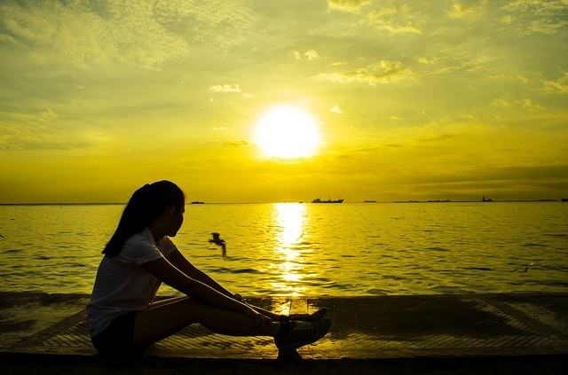 Take time to reflect Girl sitting and staring off into the sunset across the water