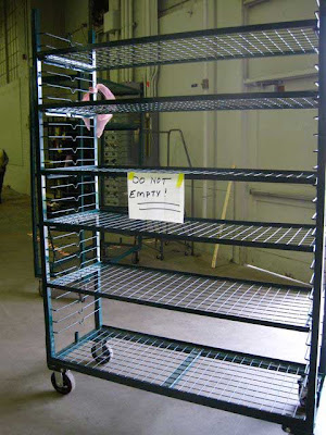 Empty green wire multi-shelves rolling cart with a hand-written sign on it that reads DO NOT EMPTY!