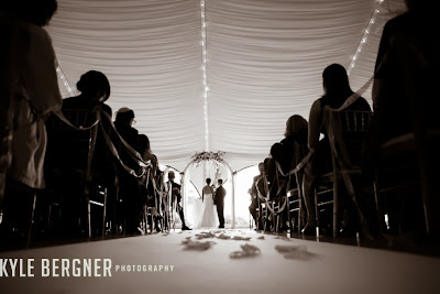 A black and white image of the bride and groom at the front of the ceremony tent