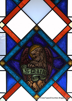 Stained glass window of winged lion with banner reading Saint Mark.