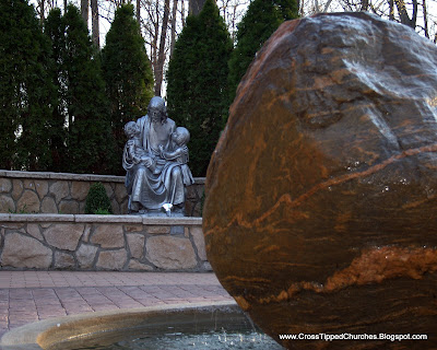Large rock fountain with the statue of Jesus holding children in the background.