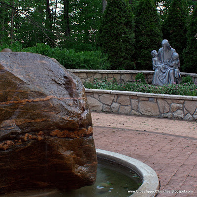 Closeup of large stone fountain with statue of Jesus holding children in the background.