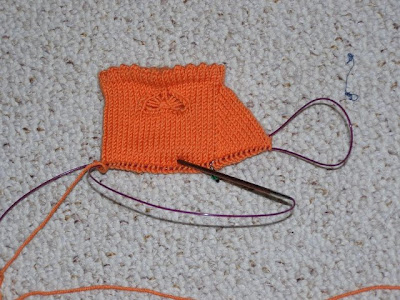 an unfinished orange sock cuff with a butterfly embellishment