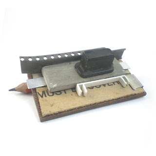 Office assemblage pin, incorporates cardboard, typewriter parts and pencil as part of pin fixture.