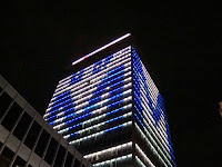 Pitch black night time view of a skyscraper with lighting that shows the University of Memphis letter M in blue with lighting that provides a white backdrop.