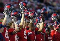 SMU football players hold up black helmets with red mustangs.