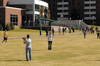students on a grass lawn walk to class in front of a brick student center.