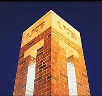 Orange illuminated red brick tower with the letters UAB inscribed atop the structure against a blue night sky background.
