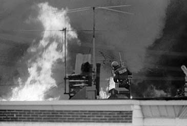 A Philadelphia police officer appears on a rooftop as flames engulf the houses around the West Philadelphia rowhouse occupied by the radical group MOVE on May 13, 1985. (AP Photo/George Widman)