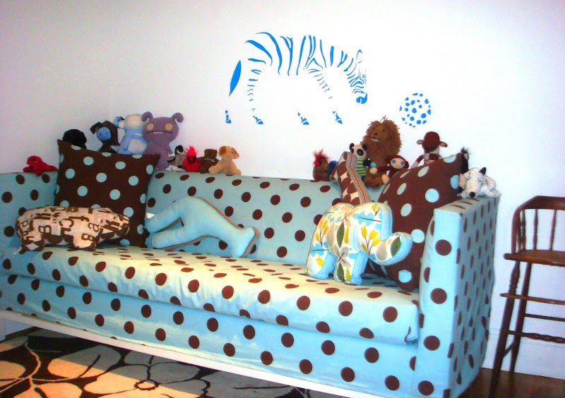 Blue and brown polka dot Jonathan Adler Lampert Sofa covered in toys in a nursery with a blue zebra playing with a ball decal