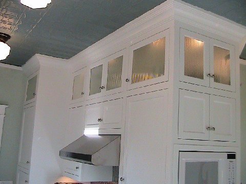 Kitchen after remodeling with white upper cabinets with reeded glass fronts and accent lights