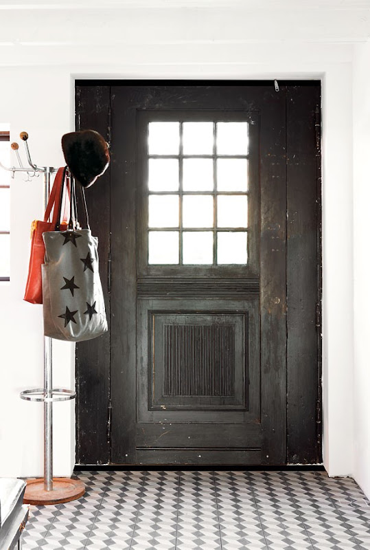 A black antique door and rough marble mosaic tile floor in a rustic entryway