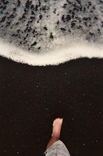 My foot buried in the jet black sand of Honokalani Beach