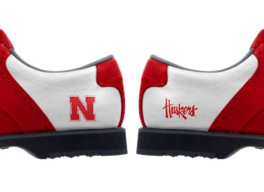 University of Nebraska golf shoes with a red letter N on one shoe and the word Huskers written on the other above black soles and cleats.