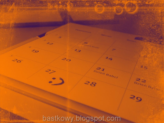 Kalendarz na ścianie z zaznaczoną uśmiechniętą buźką na 27. dniu, w tonacji ciepłej sepii