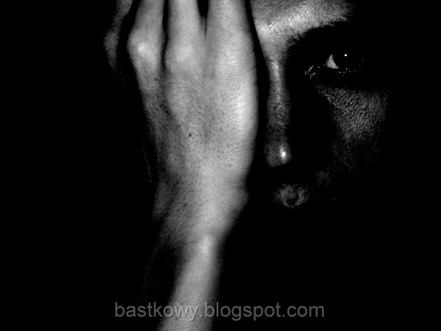 Czarno-biały portret mężczyzny, który zasłania połowę twarzy ręką, pozostawiając w tajemniczym półmroku swoje emocje i myśli