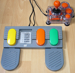 Image of a three colourful adjoined pedals and a chunky transparant joystick - accessible gaming set-up.