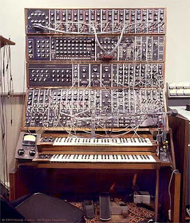 Image of a bonkers old Synthesiser with a jumbled mass of leads hanging all over it.