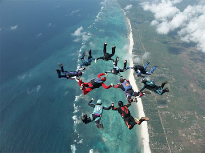 Image of 10 skydivers forming a ring falling to earth over a blue coast-line.