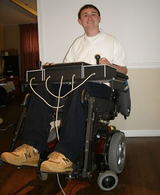 Quasicon Axis Basile. Josh Basile grinning with his large Quasicon accessible game controller, positioned on his wheelchair tray.