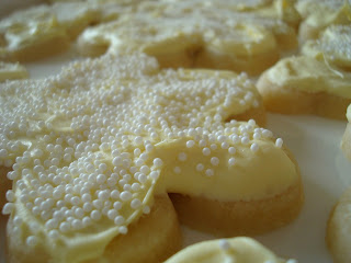 A sugar cookie frosted with yellow frosting and covered in white sprinkles. 