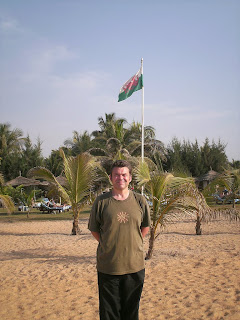 Rhys Hughes on beach in Africa with Welsh flag in background.