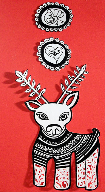 Black and white original drawing of a whimsical reindeer with paper cut out details set over a red background. It has two small ink drawings of a bird and a heart to glue to the ends of the strings to hang the reindeer with