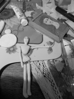 Black and white picture of my doll on the making, laying on my work area with craft related items