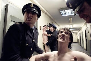 Two prisoners being hauled up a prison corridor
