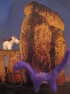tiny felt dinosaur and tinier felt pony in front of a stonehenge background
