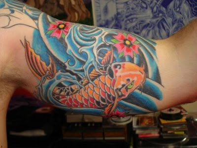 An orange koi fish tattoo in the splashing water on a young man's sleeve.