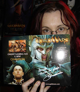 Your blogger - a woman with red hair and glasses - peers over top of a box for the game Guild Wars, which has been autographed in silver pen