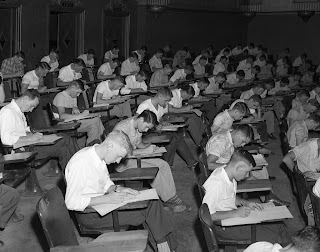 rows of students at desks writing exams