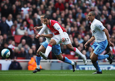 Theo Walcott of Arsenal gets a shot in while holding off the challenge of Wilfred Bouma and Curtis Davies of Aston Villa