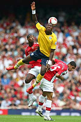 Ishmael Miller of West Bromwich Albion jumps for the ball against two Arsenal defenders.