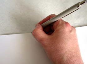 Drawing a line along the edge of a piece of cardboard onto a length of paper.