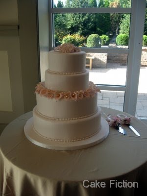 An elegant four tier wedding cake in ivory fondant surrounded by a ring of An elegant four tier wedding cake in ivory fondant surrounded by a ring of