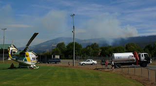 Fire-fighting helicopter at Huonville oval, having refuelled. Judds Creek Rd fire seen in background - 18 Feb 2007