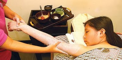 Seorang anak perempuan menikmati perawatan spa untuk tubuh. Kulitnya sedang dilumuri scrub untuk meruntuhkan kotoran