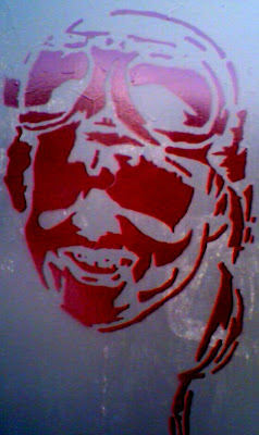 The closeup of a stenciled, in maroon paint, aviator picture with helmet and glasses on a green electric box.