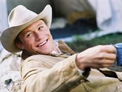 Heath Ledger usa um chapéu de caubói e sorri segurando uma caneca.