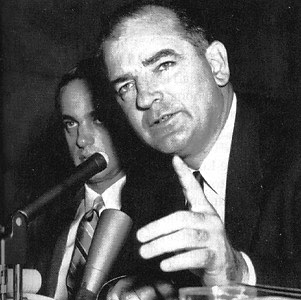 Photo of Joe McCarthy speaking at a hearing, Roy Cohn in background